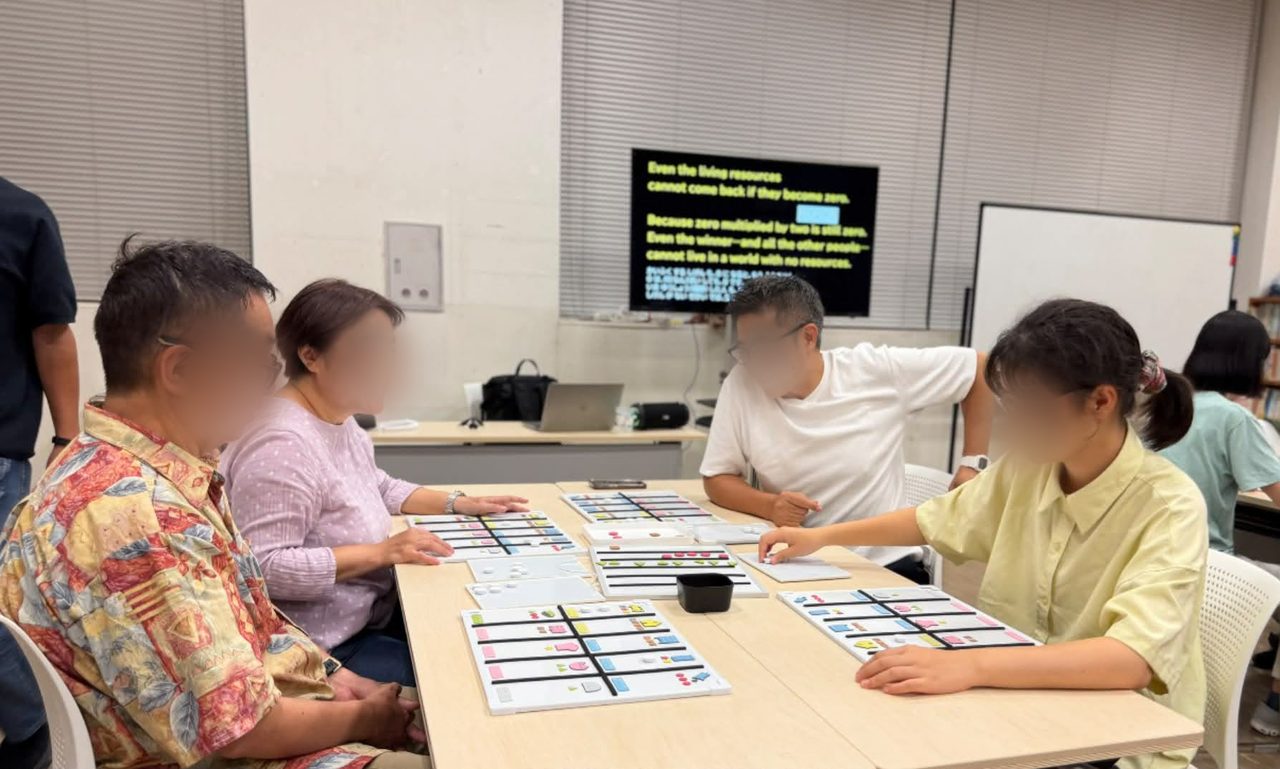 体験会のようす。4人が机を囲んで、突起のついた盤面に手を伸ばしている